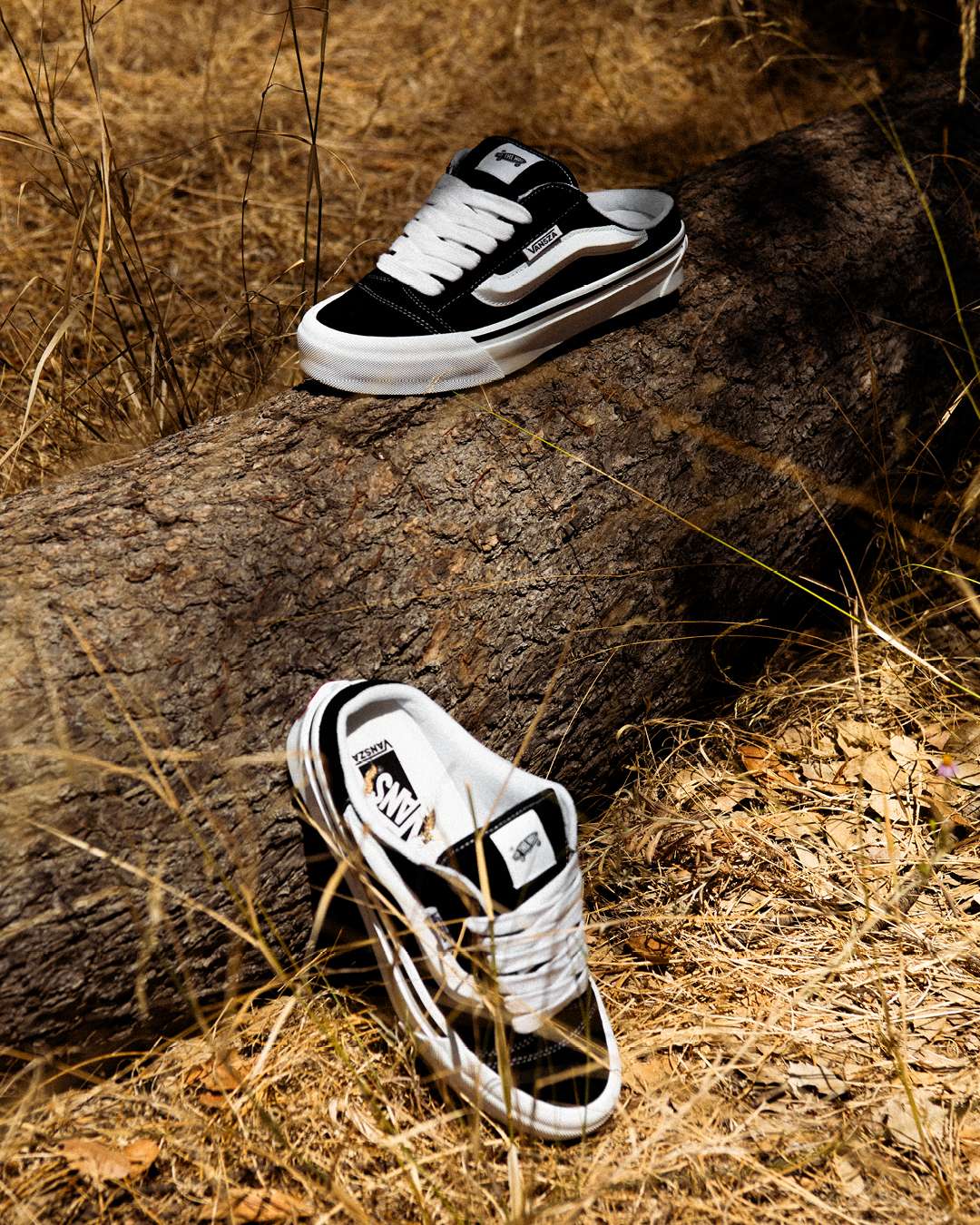 Black-and-white VANSZA Knu Skool Mule shoes placed on a fallen tree in dry grass